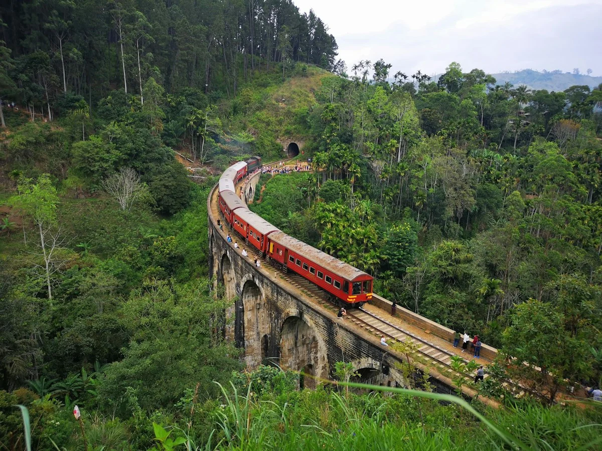 A train crossing Nine Arch Bridge amid the green hills of Ella